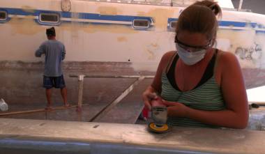 Amanda polishing the mast while Duk sands the port topsides