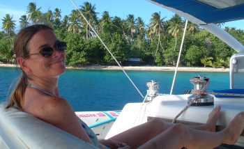 Mary relaxing in the cockpit as we sail past a small motu