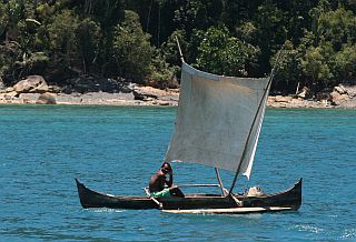 Tiny outrigger pirogue sailing happily