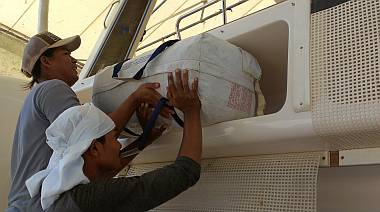 Heru and Baw lift the life-raft into its storage compartment